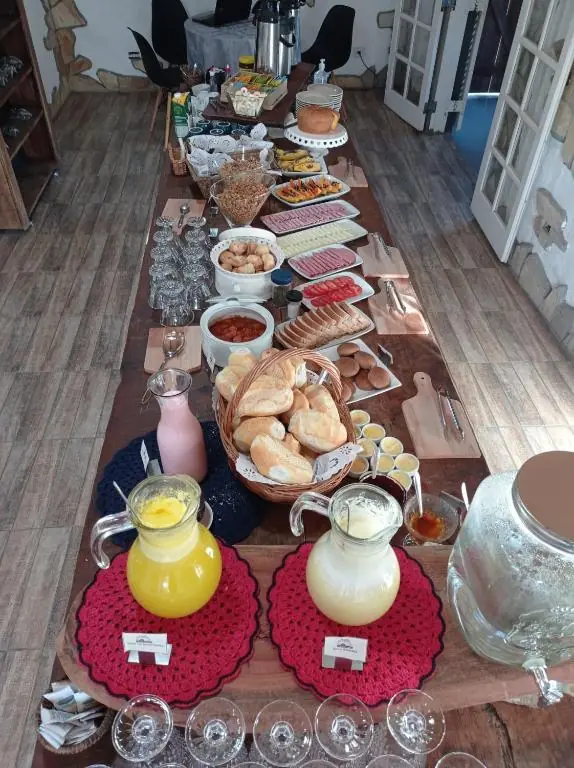 Mesa longa do café da manhã com pães, frios, frutas e sucos